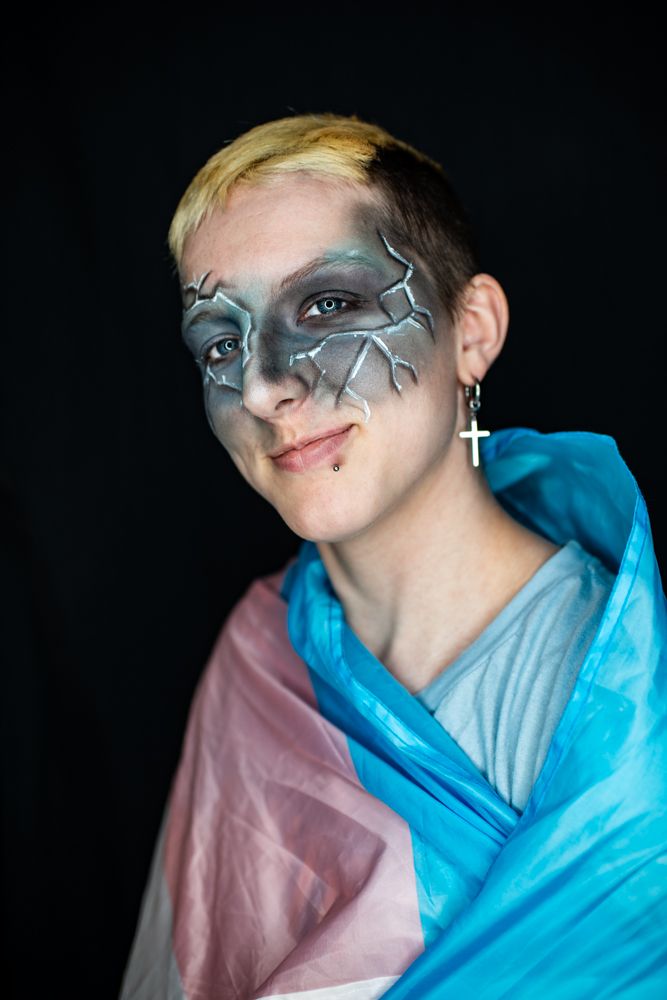 Creative portrait with silver face paint and bold turquoise and pink fabric creating dramatic contrast against dark background.