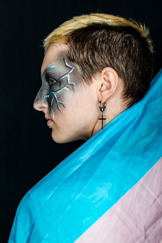 Side profile with artistic silver lightning makeup design wrapped in a vibrant blue and pink cloth against dark background.