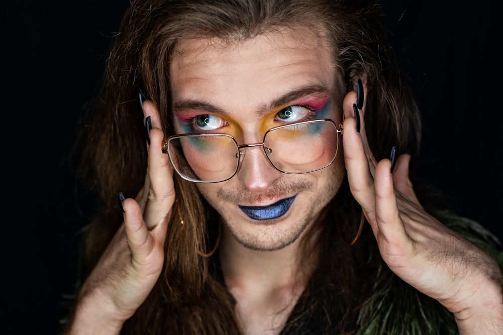 Creative fashion portraits of colorful rainbow avant-garde makeup against black background with glasses and shadows.