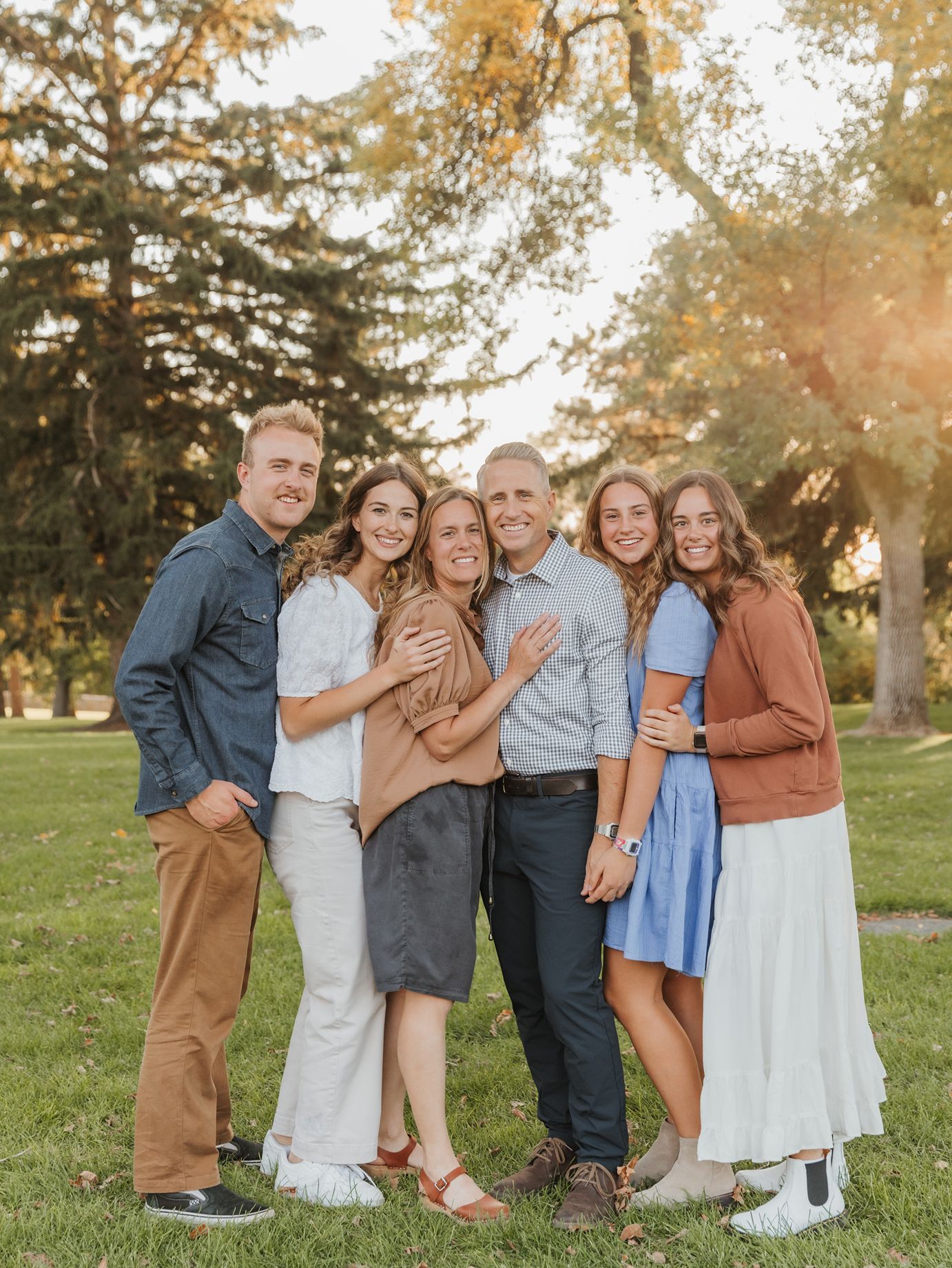 Utah county Family group in coordinated earth tones and blue dresses poses together at sunset in park setting.