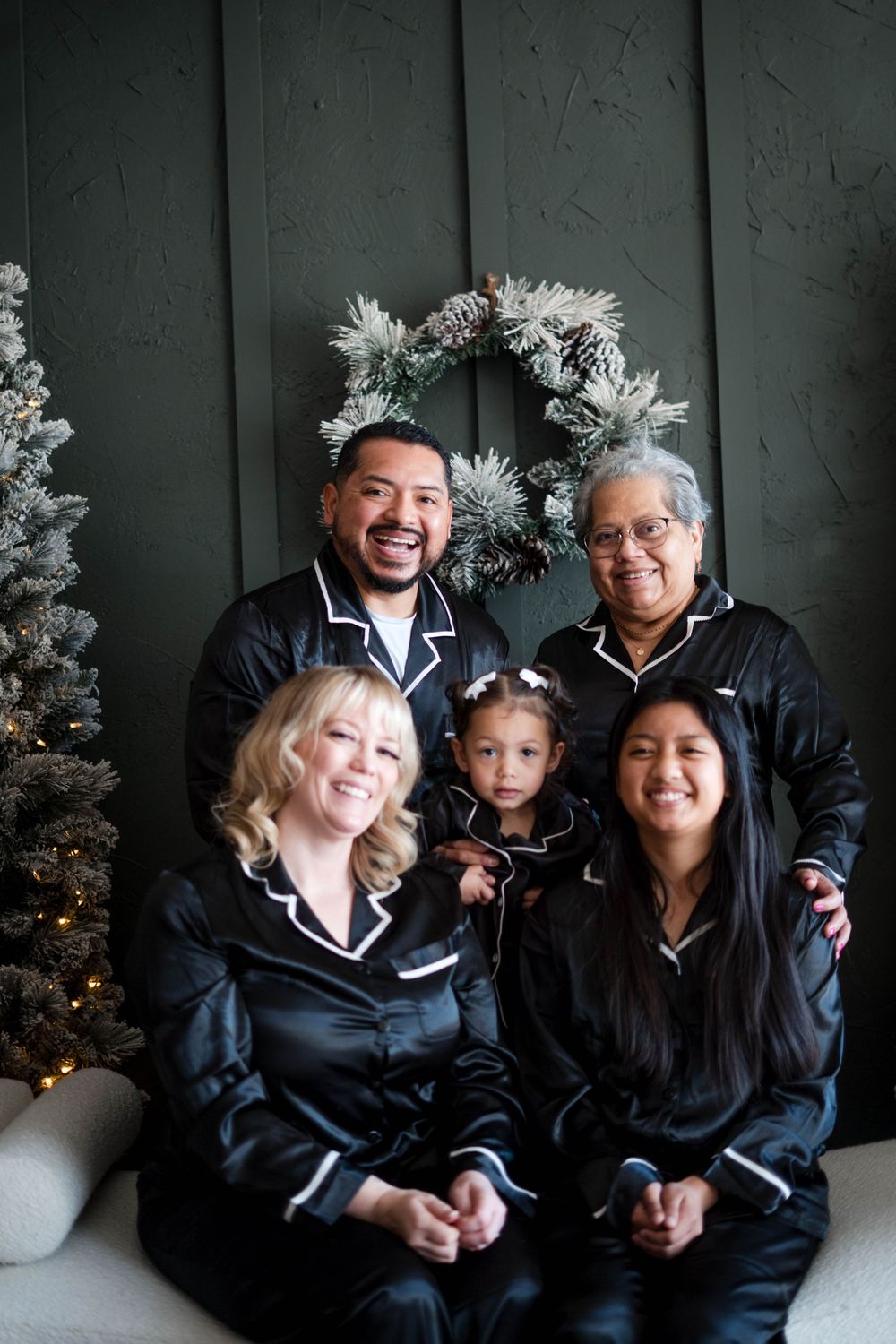 Family of five in matching black satin pajamas smile together in a festive Christmas photo session.