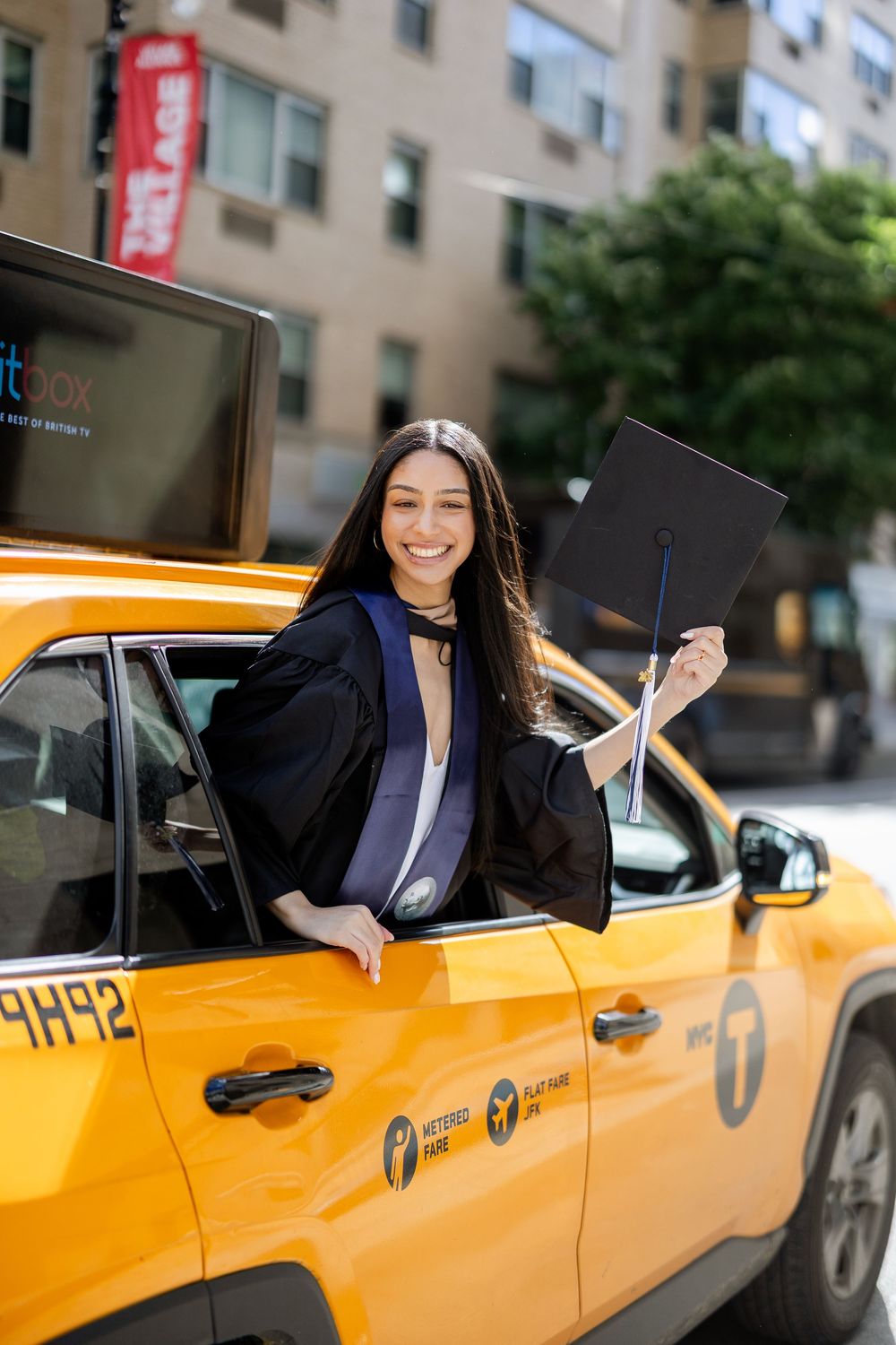 Professional woman in business attire smiles from inside a yellow New York City taxi cab on a city street.