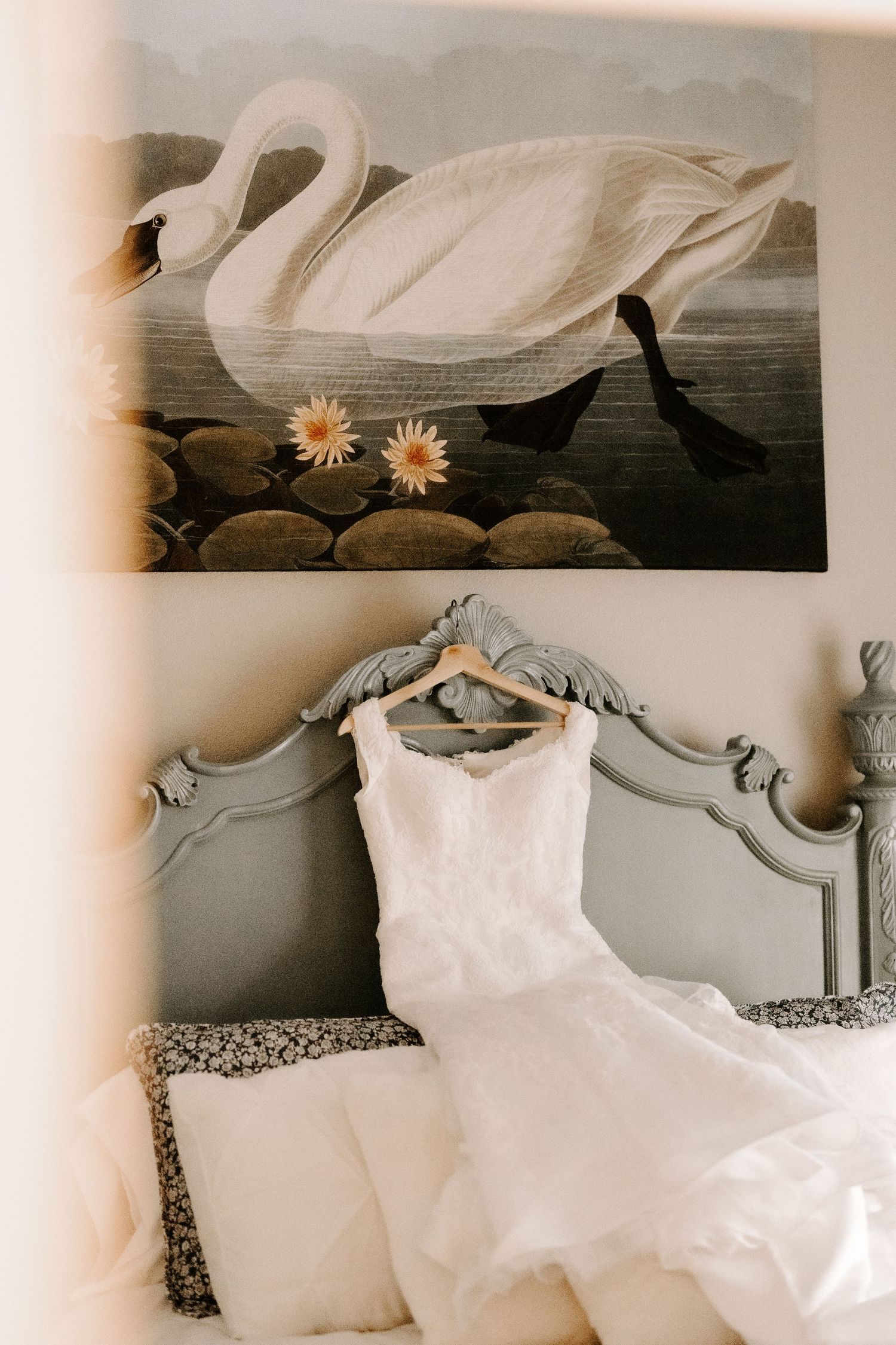 Wedding dress displayed beneath vintage swan artwork in an elegant bedroom setting.