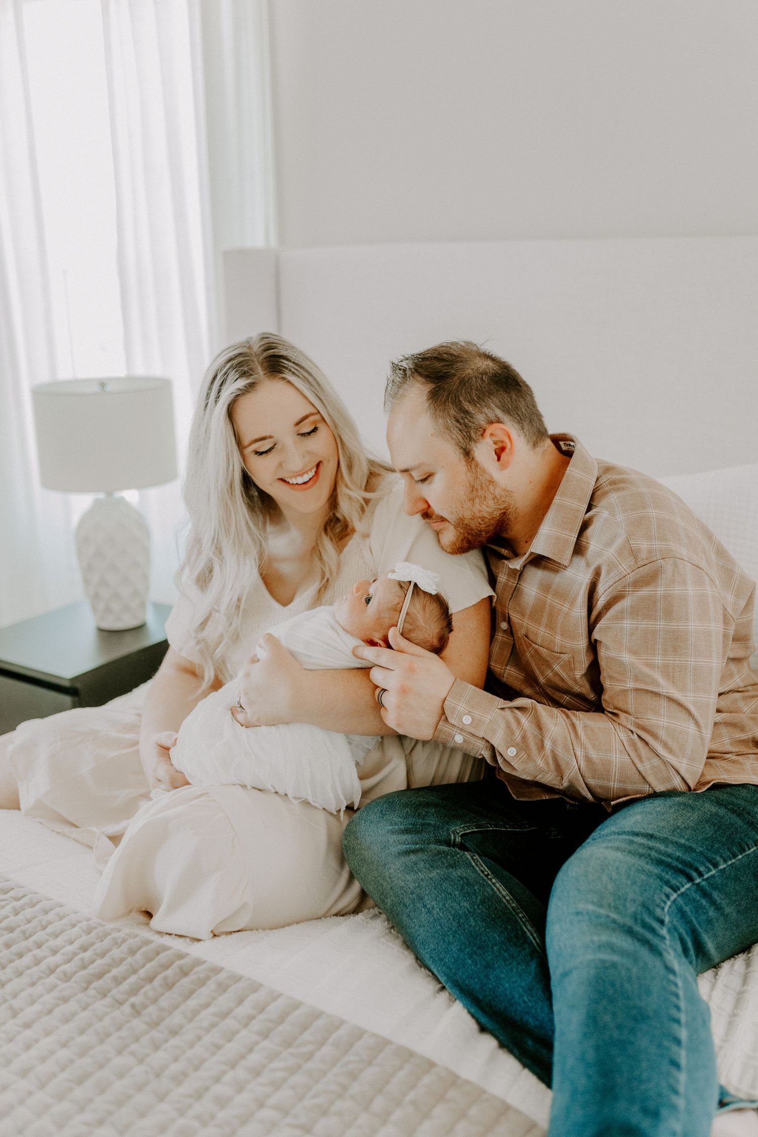 Tender family moment with newborn baby on white bedding in bright room.