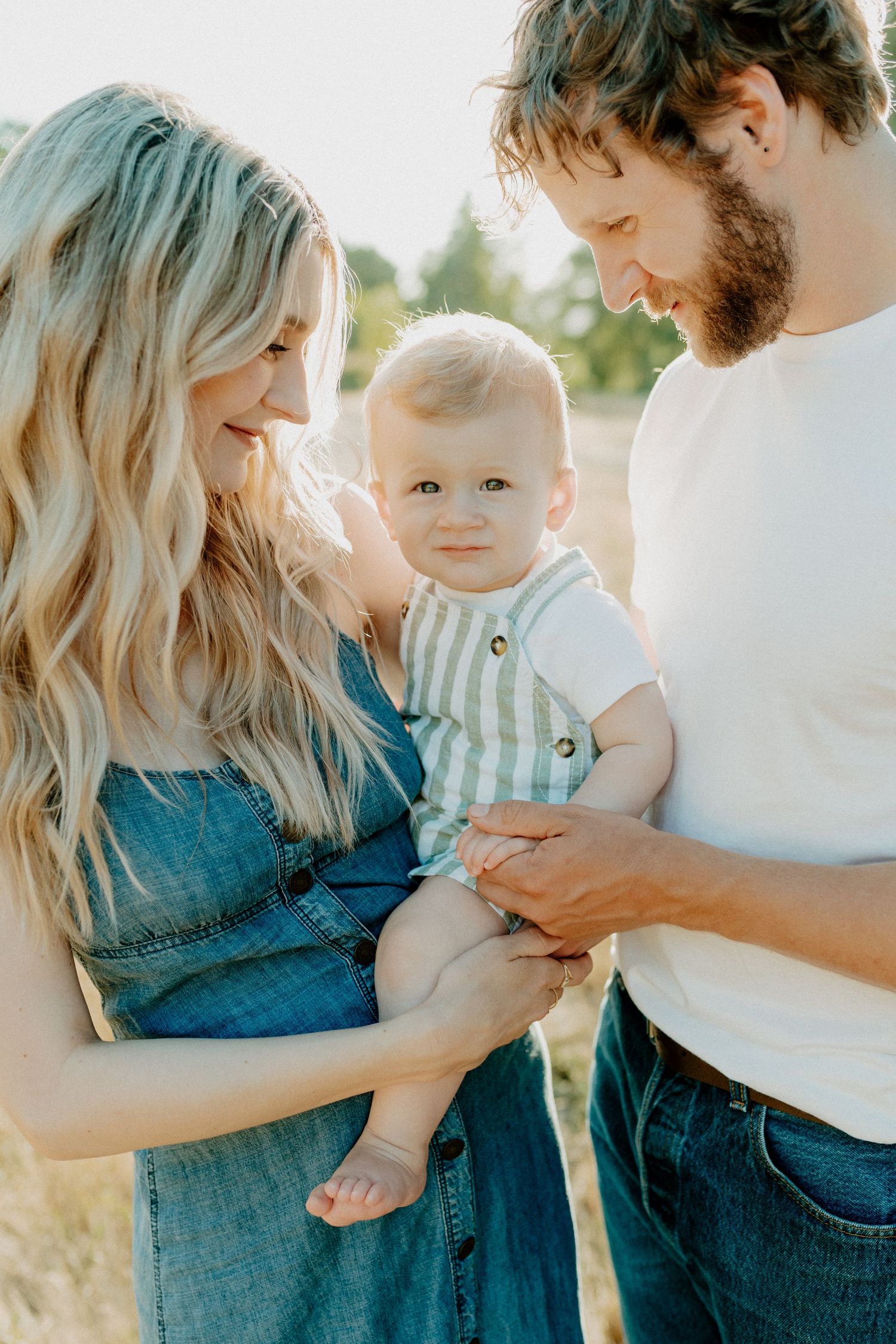 Family moment outdoors with baby in striped outfit and parents in casual wear.