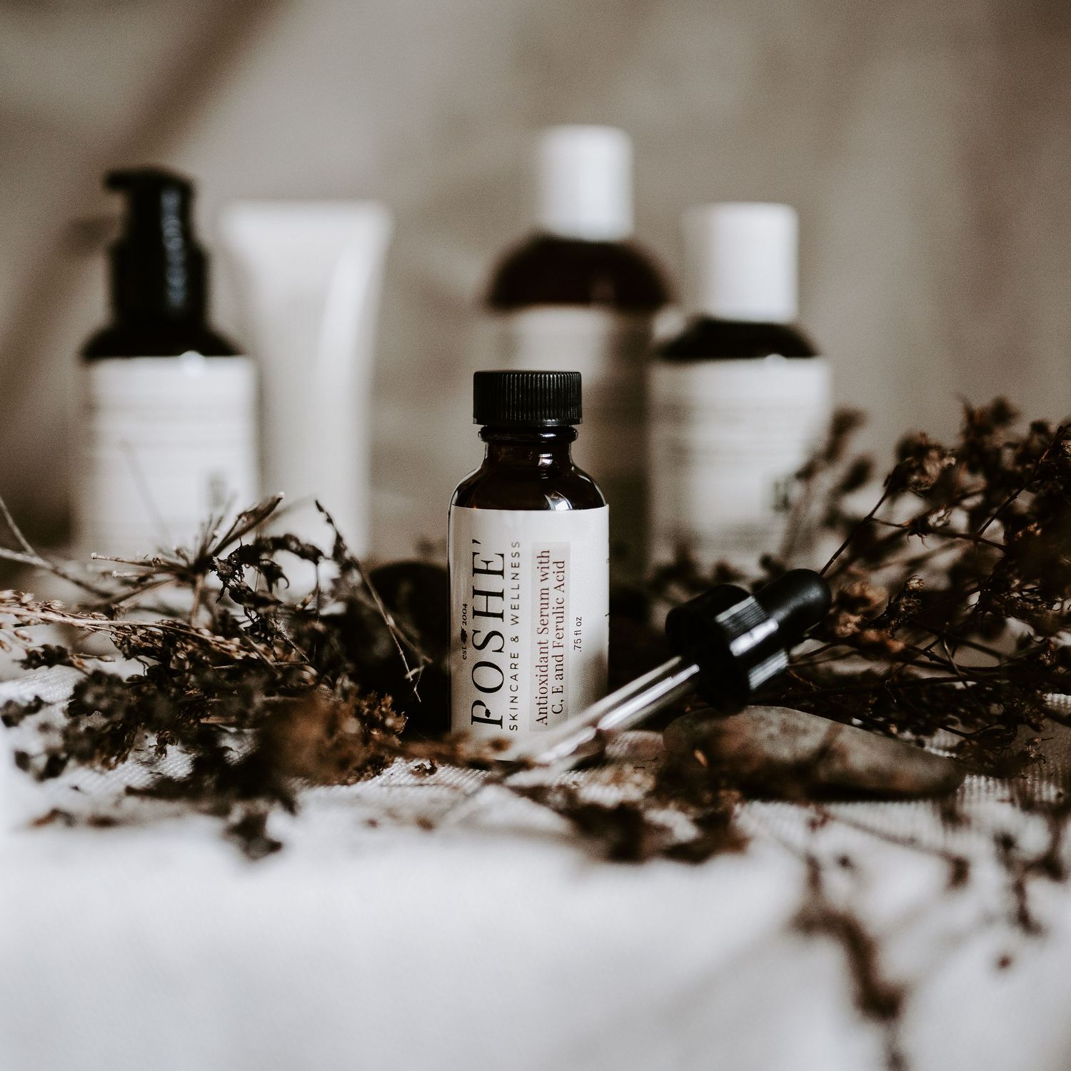 Collection of natural skincare products and essential oils arranged with dried botanicals.