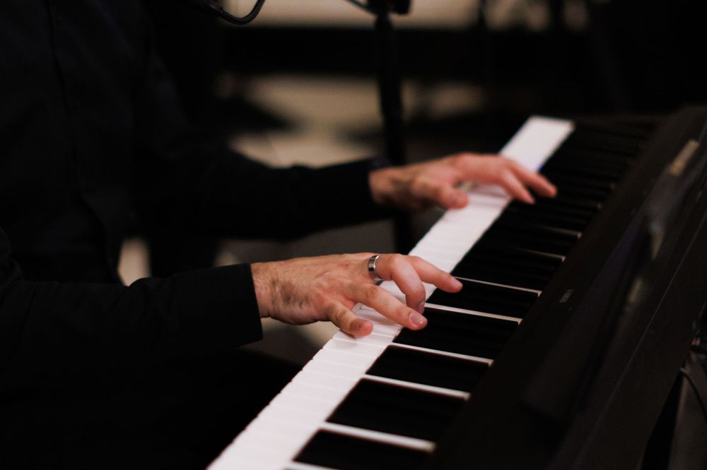 Close-up of hands wearing a ring playing a digital keyboard piano at a live performance.