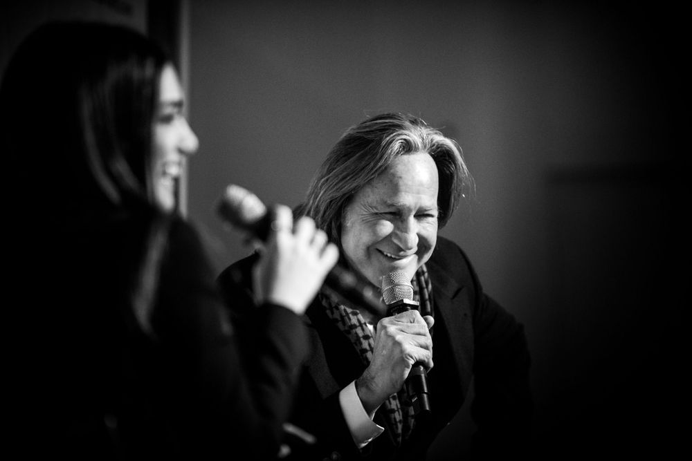 Two people sharing a laugh while holding microphones at a professional event in black and white.