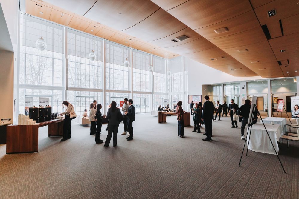 Professionals networking in a modern conference center lobby with large floor-to-ceiling windows.