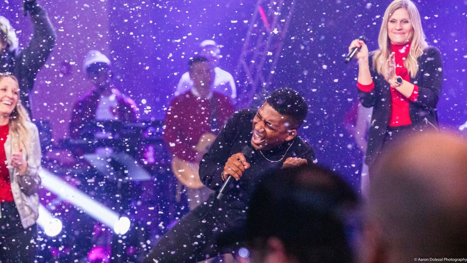 Performers on stage surrounded by purple lighting and falling confetti during an energetic concert performance.