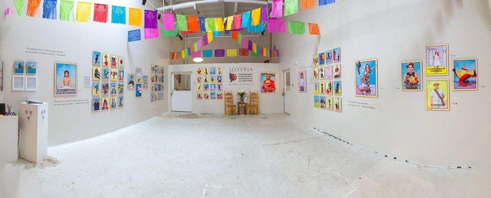 Art gallery wall displays colorful children's drawings and artwork with bright papel picado banners hanging overhead.