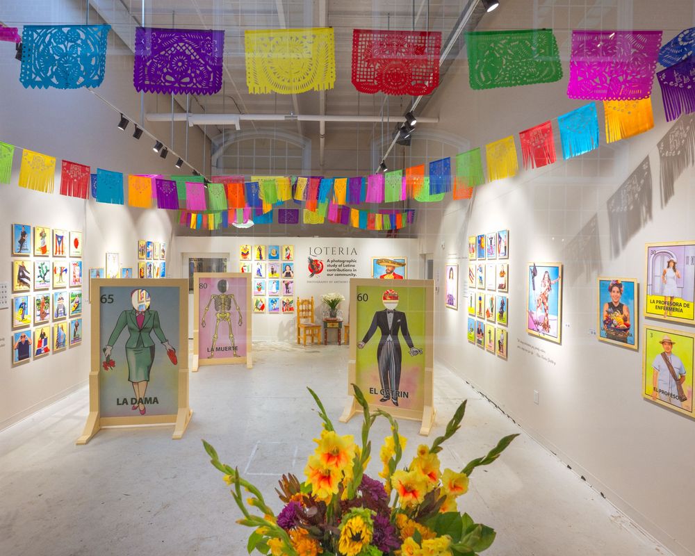 Colorful papel picado banners and student artwork hang in a bright school hallway gallery display.