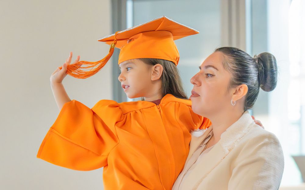 Graduates in orange caps and gowns adjust their mortarboards before commencement ceremony.