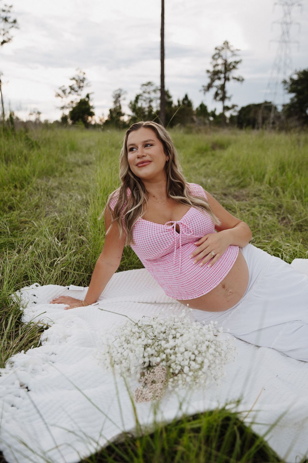 A person lounges on a white blanket in grass with baby's breath flowers wearing a pink crop top.