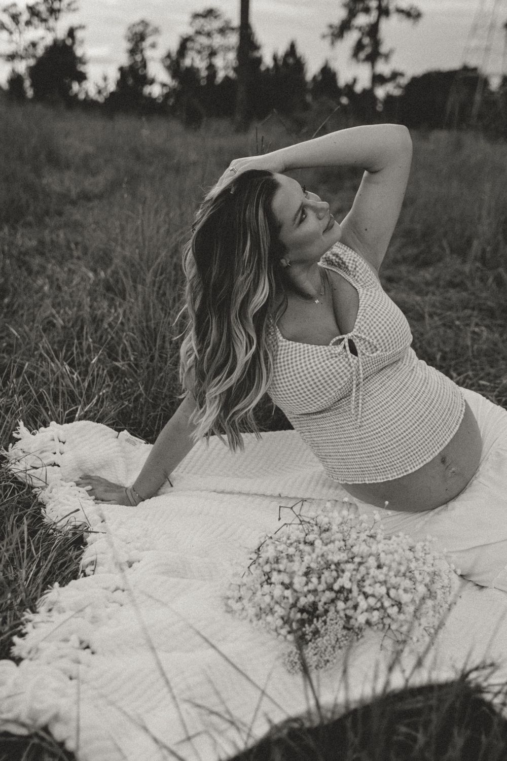 Black and white artistic portrait of someone laying in a field with white flowers wearing a polka dot dress.