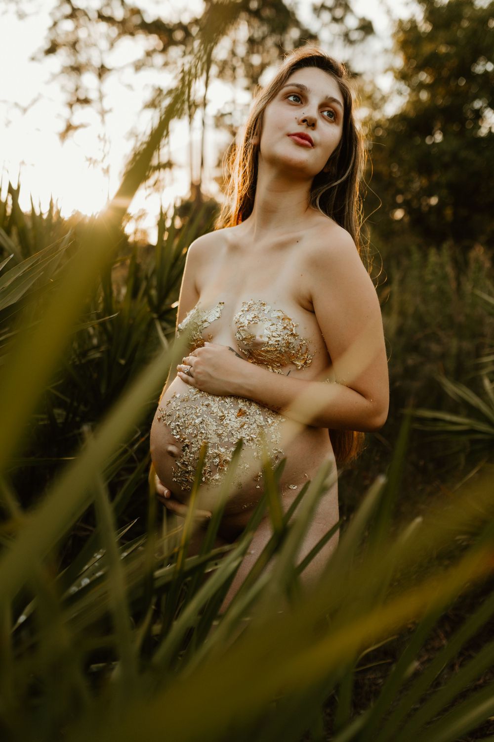 Ethereal maternity portrait amid palm fronds with golden sunlight streaming through.