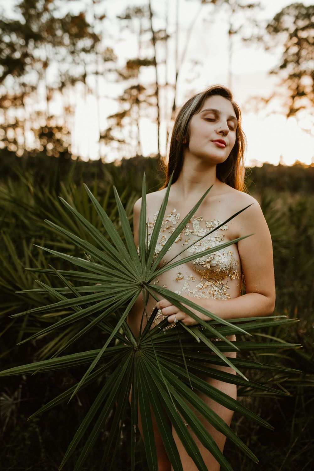 Artistic maternity photo with tropical palm fronds and sunset lighting.