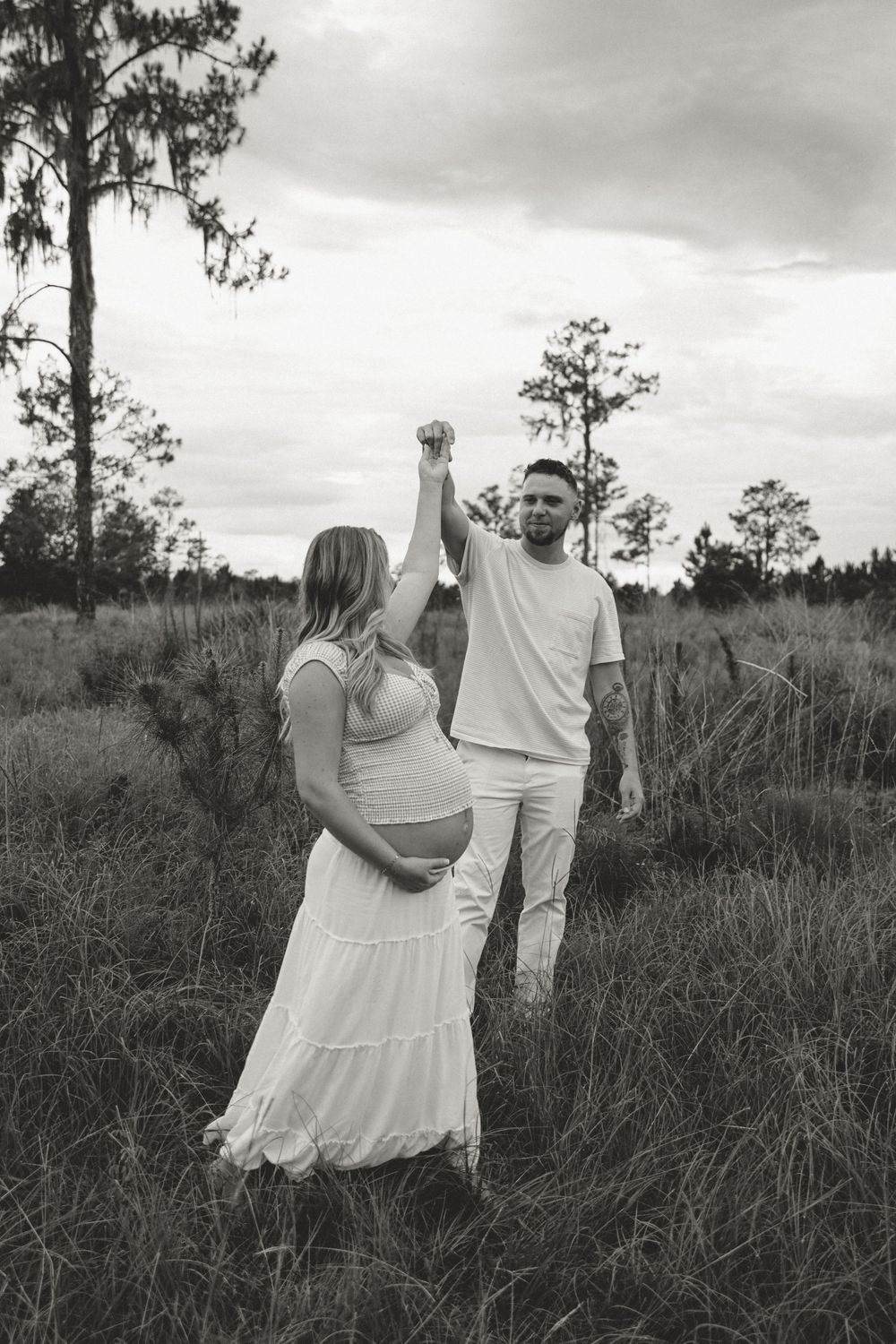 Black and white panorama sequence showing couple in white outfits walking through tall grass in a natural setting.