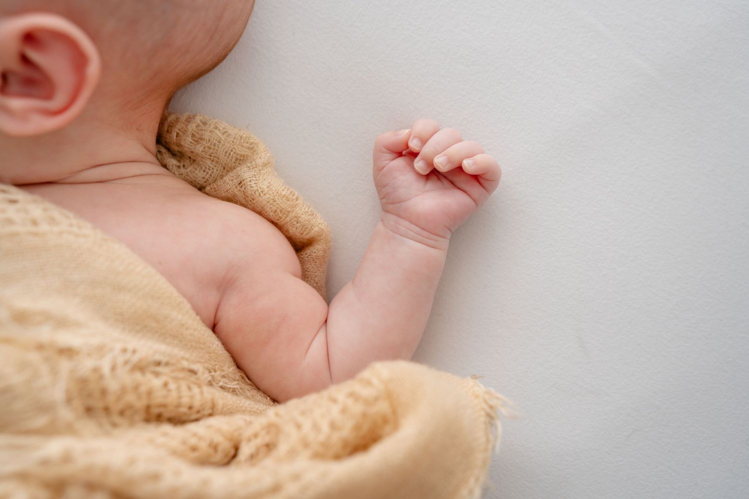 Close-up of newborn baby feet wrapped in soft beige blanket.
