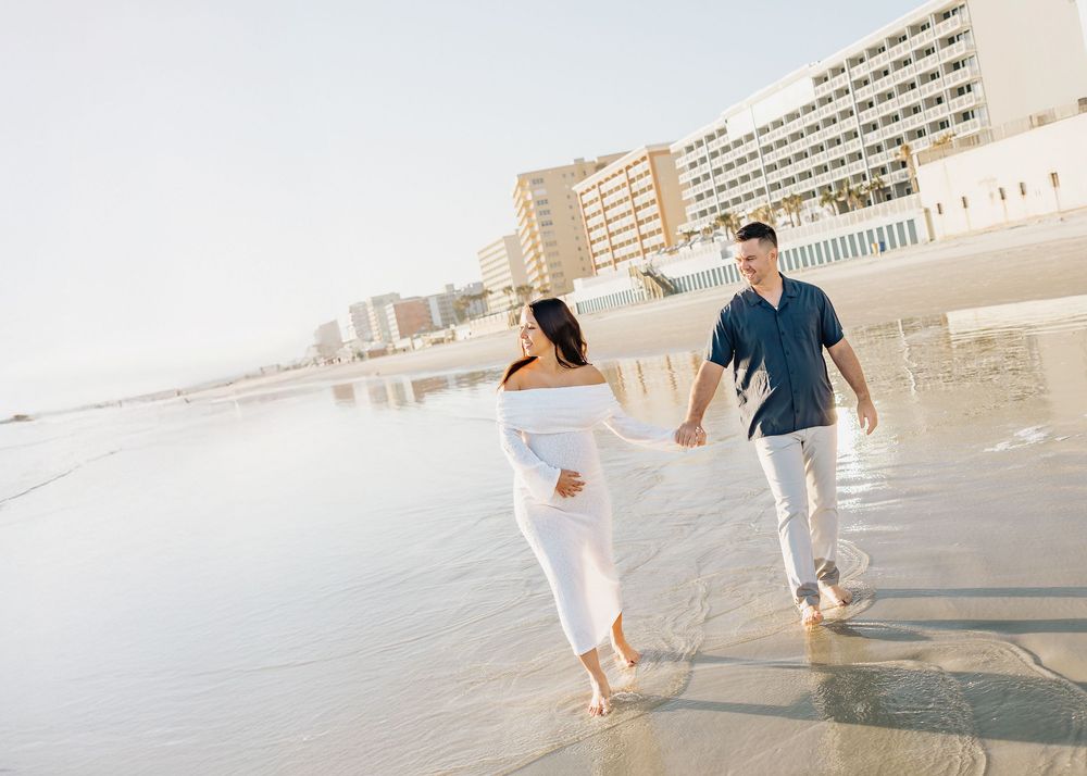 Couple walking and playing together on a sunny beach with waves in the background.