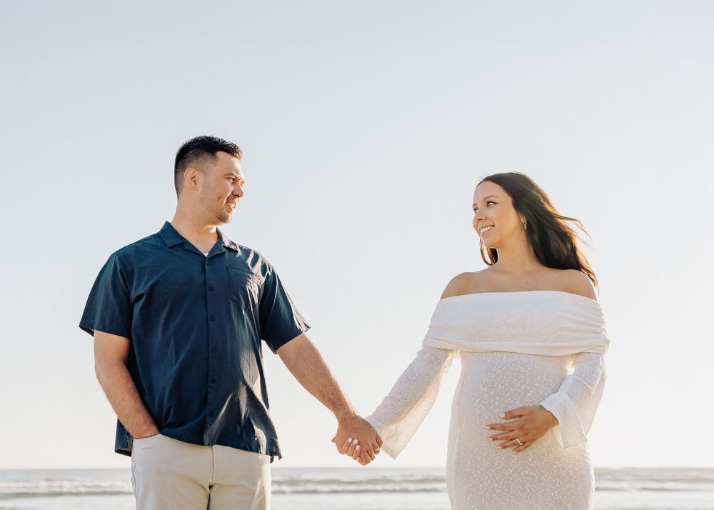 Couple holding hands and walking along a bright sandy beach in casual attire.