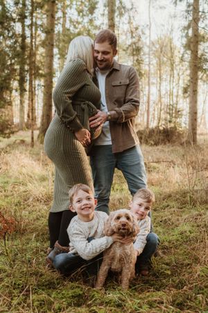 Family and their dog posing playfully among tall trees in a forest setting.