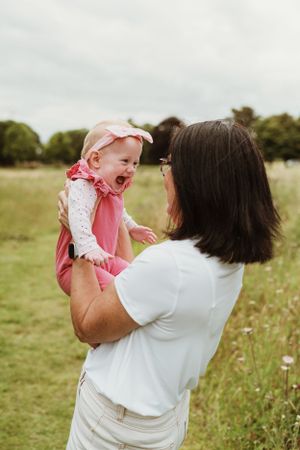 A joyful moment captured in a grassy field as a parent lifts and spins a small child wearing pink.