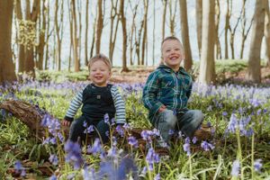Family sitting among purple bluebells in sunlit spring forest.