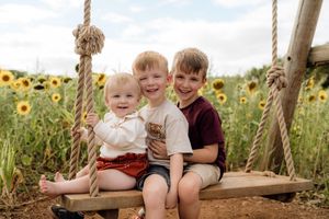 Children sit together on a wooden swing in a vibrant sunflower field during golden hour.
