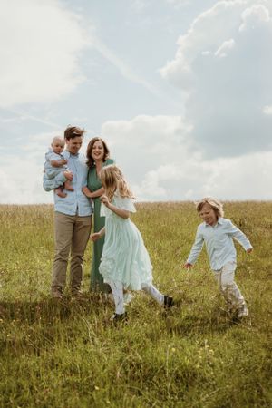 A family runs and plays together in a grassy field on a bright summer day.
