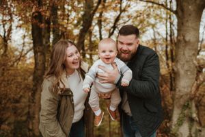 Autumn outdoor family portrait with golden leaves and trees in background.