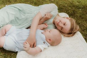 A child rests peacefully on a white blanket in a field of grass.