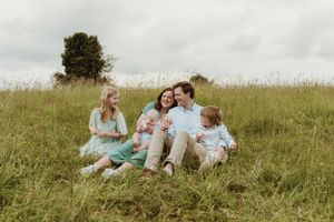 A family relaxes together on a grassy hillside during a sunny afternoon.