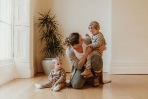 Family bonding moment on white floor with indoor plants in bright minimalist setting.