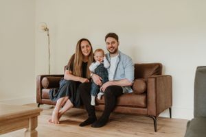 Family relaxing together on a brown leather couch in a minimalist living room.
