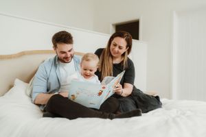 Family lounging together on white bedding in bright room.
