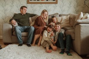 Family lounging together on a gray couch with floral wallpaper backdrop.