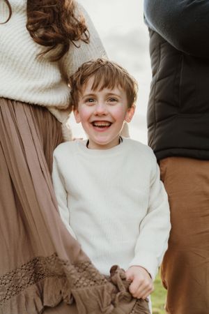 Child wearing white sweater smiling joyfully during outdoor photo session.