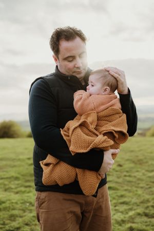 Parent and child sharing tender moment outdoors in brown and black clothing.