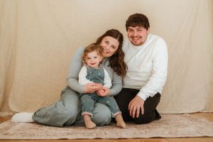 Family enjoying playful moments together on a light beige backdrop in coordinated casual outfits.