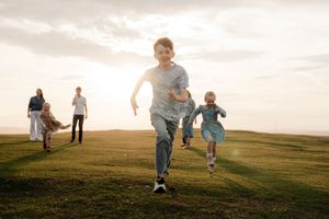 People running up a grassy hill against a sunset sky during golden hour.