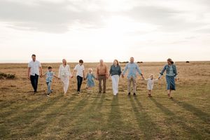 Group in white and blue outfits walking together across a grassy hillside during sunset.