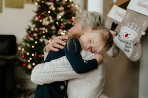 Intimate family gathering showing affectionate embrace on couch during holiday season with Christmas tree lights glowing.