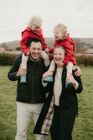 Happy family enjoying outdoor playtime with children riding on shoulders against an autumn landscape.