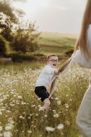Child playing joyfully in a sunlit meadow filled with white wildflowers at golden hour.