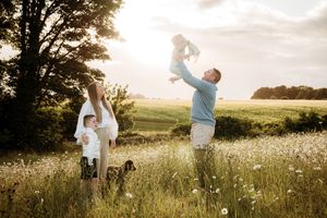 Playful family photoshoot in a golden meadow during sunset.