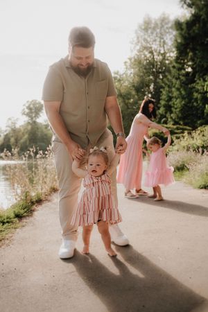 A family walks along a sunlit path on a summer evening wearing coordinated pink and beige outfits.