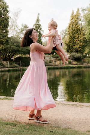 A pair in matching pink dresses share playful moments by a serene pond on a sunny afternoon.