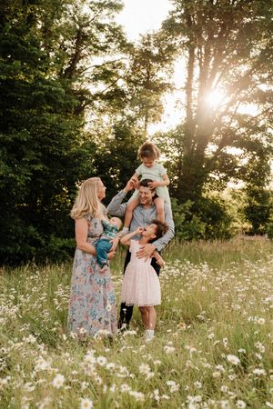Family enjoying a playful moment together in a field of white wildflowers at sunset.