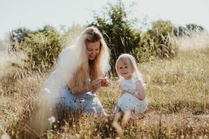 A family sits together in a sunlit meadow surrounded by tall grass and wildflowers on a warm afternoon.